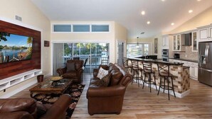 A spacious living room with a large TV, leather sofas, and a dining area with bar stools. - 3/2 Home steps away from Tiger Tail access (Marco Island)