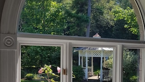 Uitzicht door een raam op een tuin, een prieeltje en een roze bloem.