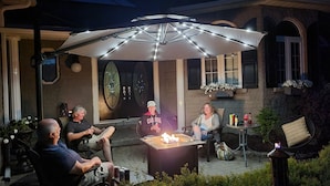 Een terras buiten met een vuurkorf, zitplaatsen en een parasol.