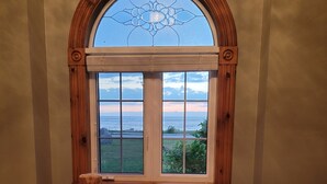 Een kamer met een groot rondboogvenster met uitzicht op een schilderachtig panorama, een houten bankje met een pluizig vloerkleed, en een stapel handdoeken op het bankje.