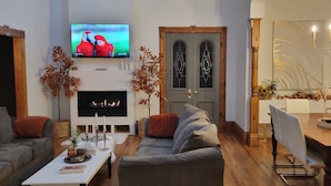 Een woonkamer met een open haard, een televisie en een eetgedeelte met een kroonluchter.