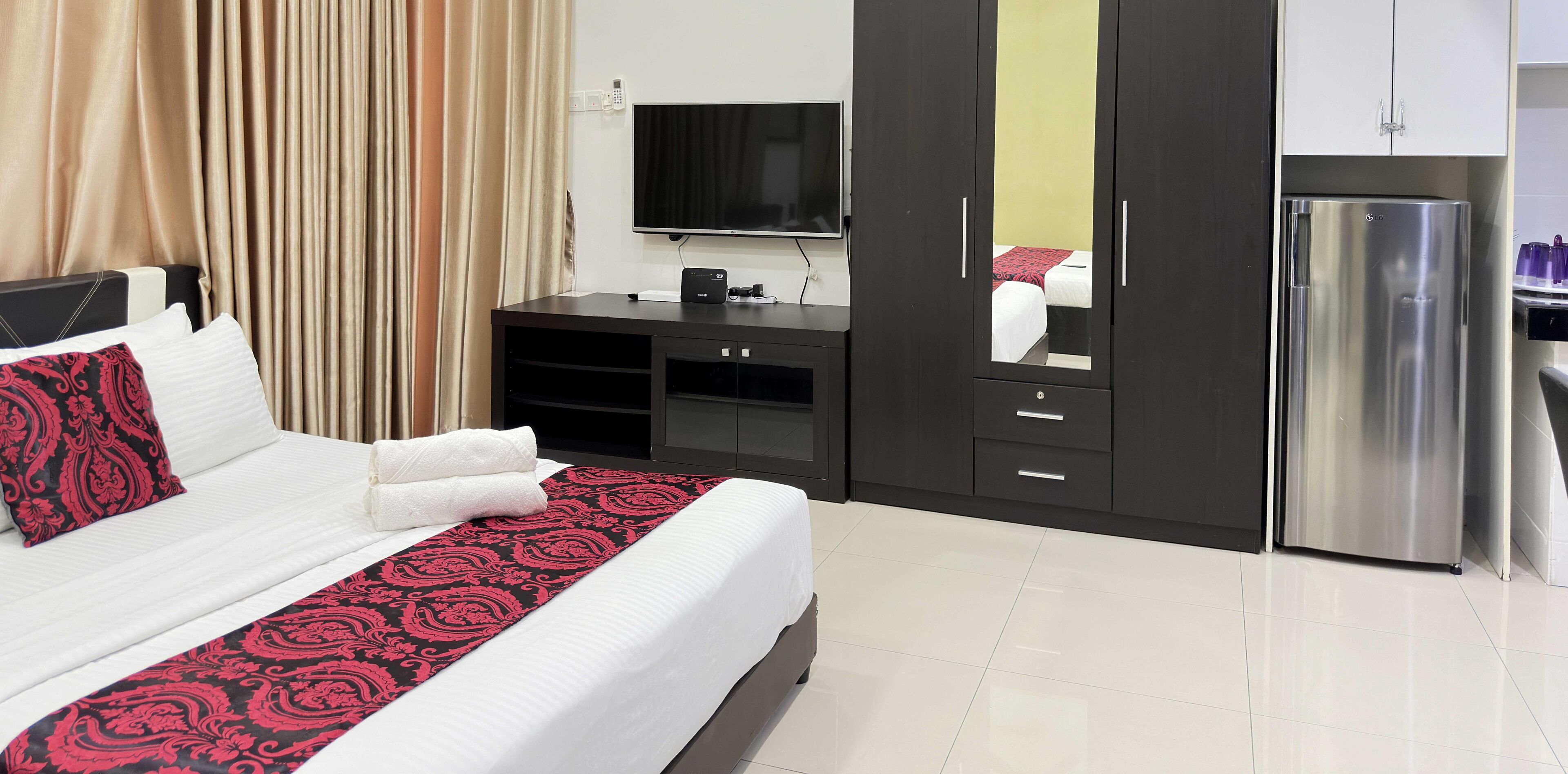 Habitación de hotel con cama, televisor, minibar y refrigerador.