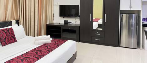 A hotel room with a bed, a TV, a minibar, and a refrigerator.