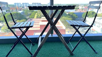 A pair of foldable chairs with a table in front, positioned on a green carpeted floor with a view of a cityscape through a window.
