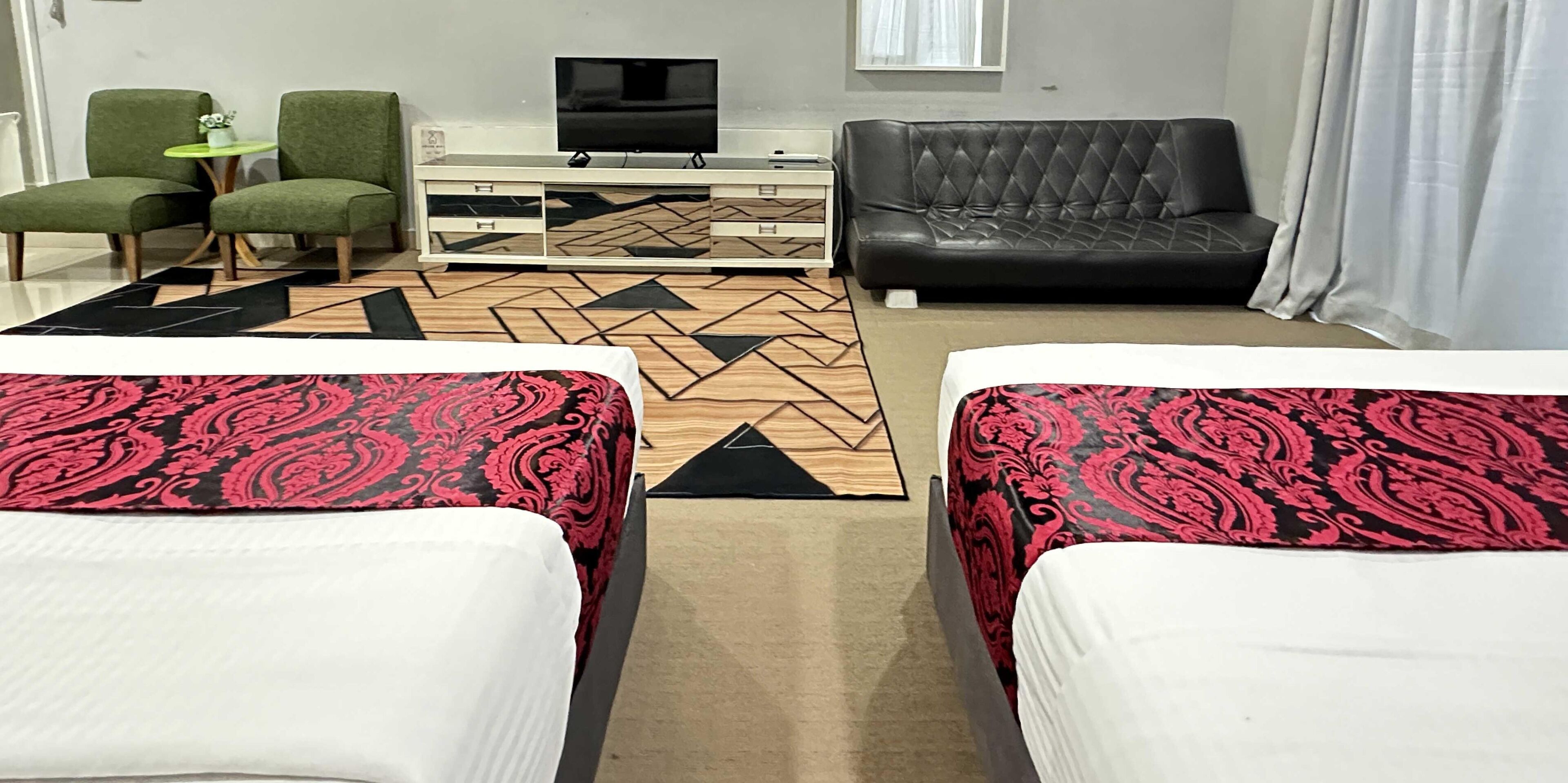 A hotel room with two beds, a sofa, a TV, and a small table with a plant.