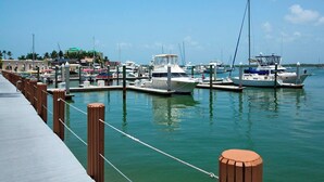 A marina with boats docked at wooden piers, a concrete walkway, and buildings in the background. - Lovely condo on the Bay with inland view! (Marco Island)
