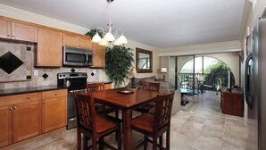 A spacious kitchen with wooden cabinets, a dining table, and chairs. There is a large window providing natural light and a view of the outdoors. - Lovely condo on the Bay with inland view! (Marco Island)