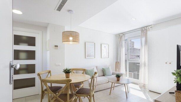Een moderne woonkamer met een eettafel, stoelen, een bank, een groot raam en een televisie.