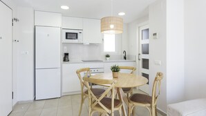 Een moderne keuken met witte kasten, een ingebouwde magnetron, een koffiezetapparaat, en een eethoek met een ronde houten tafel en vier houten stoelen.