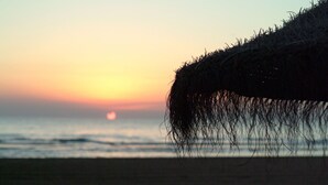 Een strandscène bij zonsondergang, met een rieten voorwerp op de voorgrond.