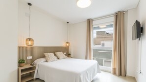 Een moderne slaapkamer met een bed, nachtkastjes, een kleine plant en een aan de muur bevestigde televisie.