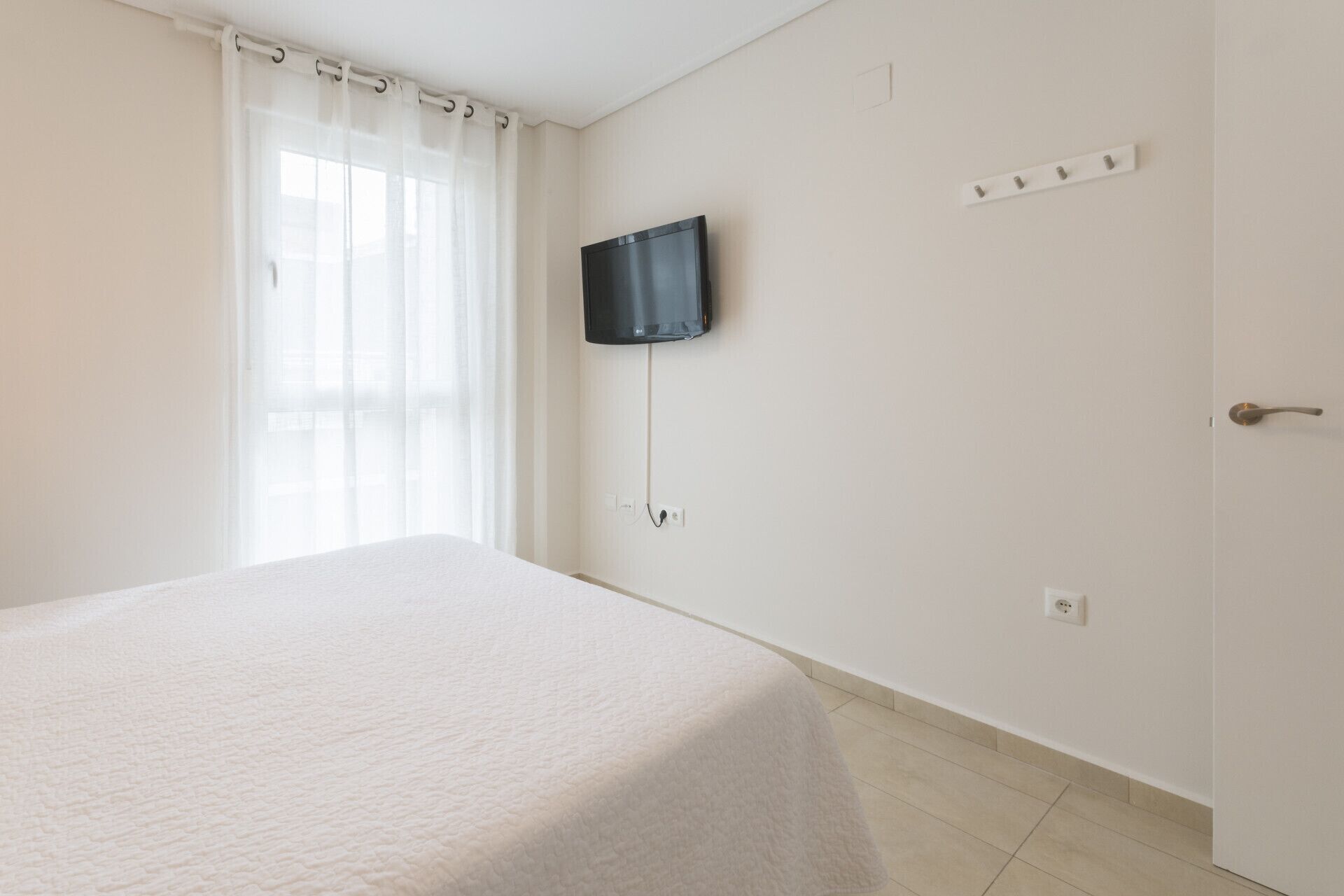 A room with a bed, a television mounted on the wall, and a door with a handle.