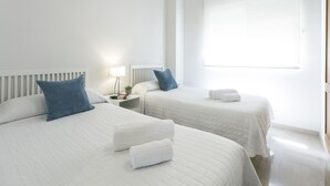 Une chambre d’hôtel avec deux lits, du linge de lit blanc, une table de chevet avec une lampe et une fenêtre.