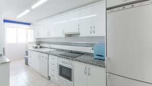 Une cuisine moderne avec des armoires blanches, un comptoir en granit, un four encastré et un réfrigérateur.