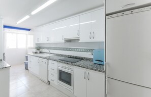 Cozinha moderna com armários brancos, bancada de granito, forno embutido e geladeira.