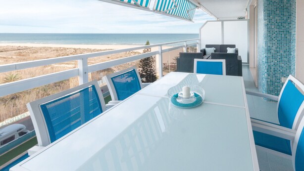 Un balcon avec vue sur la plage, une table avec des chaises et un coin salon avec vue sur l’océan.