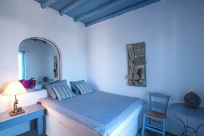 A bedroom with a bed, a chair, a small table, a lamp, and a mirror.