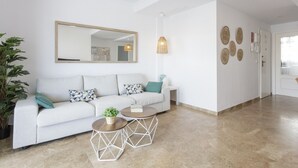 Uma sala de estar moderna com um sofá branco, duas mesas redondas, um espelho grande e decoração na parede.