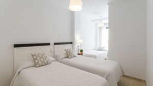 Een hotelkamer met twee eenpersoonsbedden, een nachtkastje met een lamp, en uitzicht op de gang.
