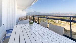 A balcony with a white table and chairs, a potted plant, and a view of mountains and a road. - Beautiful condo family near to the beach. Pool / Wifi  - only families (Playa de Gandía)