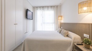 Ein Hotelzimmer mit Bett, Wand-Fernseher, Nachttischlampe und einem Fenster mit Vorhängen.