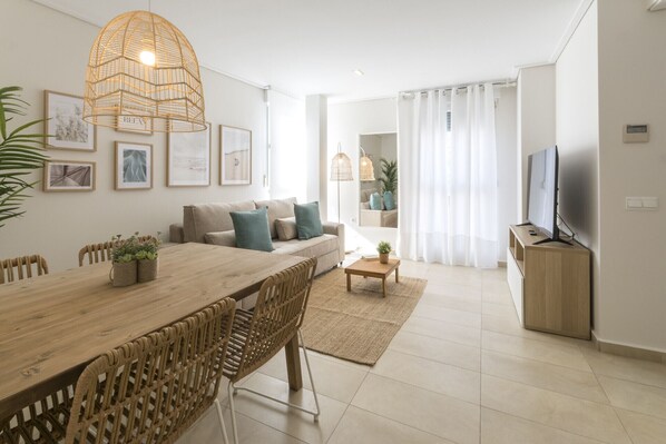 Un salon moderne avec une table à manger en bois, un canapé beige et un téléviseur posé sur un meuble en bois.