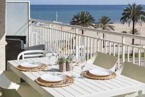 Un balcon avec une table blanche dressée pour deux personnes, donnant sur une plage bordée de palmiers et sur l’océan.
