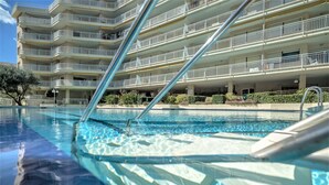 A swimming pool with clear blue water, surrounded by a multi-story building with balconies. - Apartment with amazing Ocean Views / Pool - Only families (Playa de Gandía)