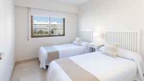 A hotel room with two beds, a window with a view of buildings, a bedside table with a lamp, and a radiator. - Apartment with amazing Ocean Views / Pool - Only families (Playa de Gandía)