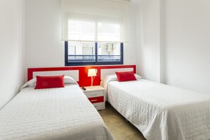 Two single beds with white bedding and red accents, each with a nightstand and lamp.