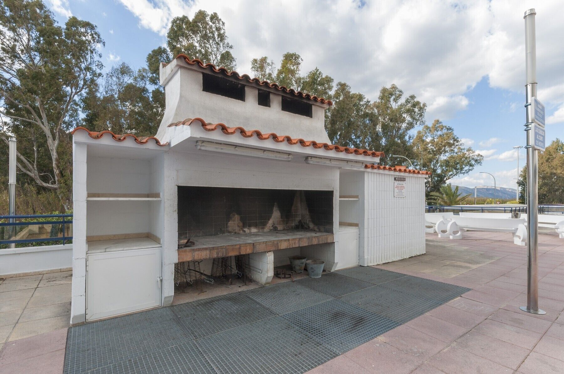 A small outdoor barbecue area with a tiled roof, a grill, and a metal grate.