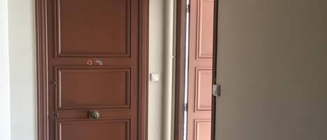 A hallway with a brown door, a white wall, and a tiled floor.