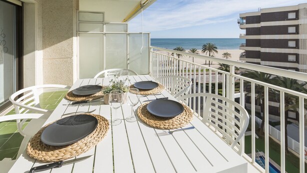 Un balcon avec une table dressée pour quatre personnes, donnant sur une plage et une piscine.