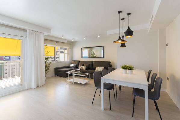 Una sala de estar moderna con un sofá, una mesa de comedor con sillas e iluminación colgante.