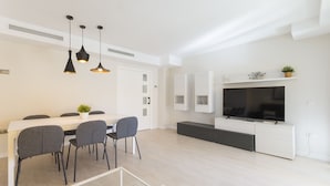 Un salon moderne avec un coin repas, des murs blancs et un téléviseur à écran plat fixé au mur.