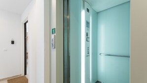A modern elevator with a metallic handrail and a green emergency exit sign.