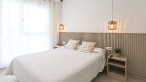 A modern hotel room with a large bed, two bedside tables, a nightstand, and a wall-mounted light fixture.