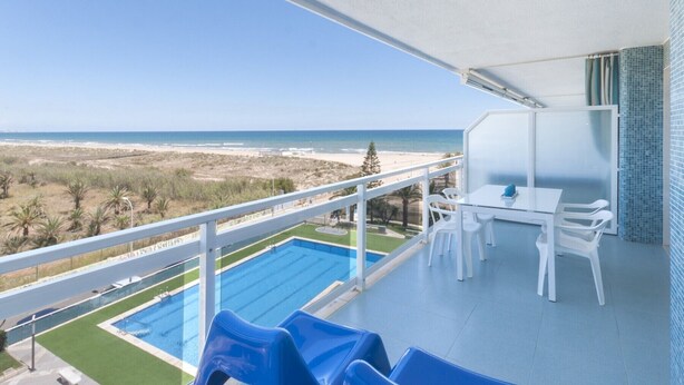Ein Balkon mit Pool, weißen Möbeln und Blick auf den Strand.