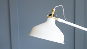 Eine weiße Lampe mit goldfarbenem Detail an einer weißen Wand.