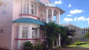 Un edificio rosa y blanco con balcón, columnas y jardín.