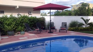 Piscina con sillas de descanso y una sombrilla roja.