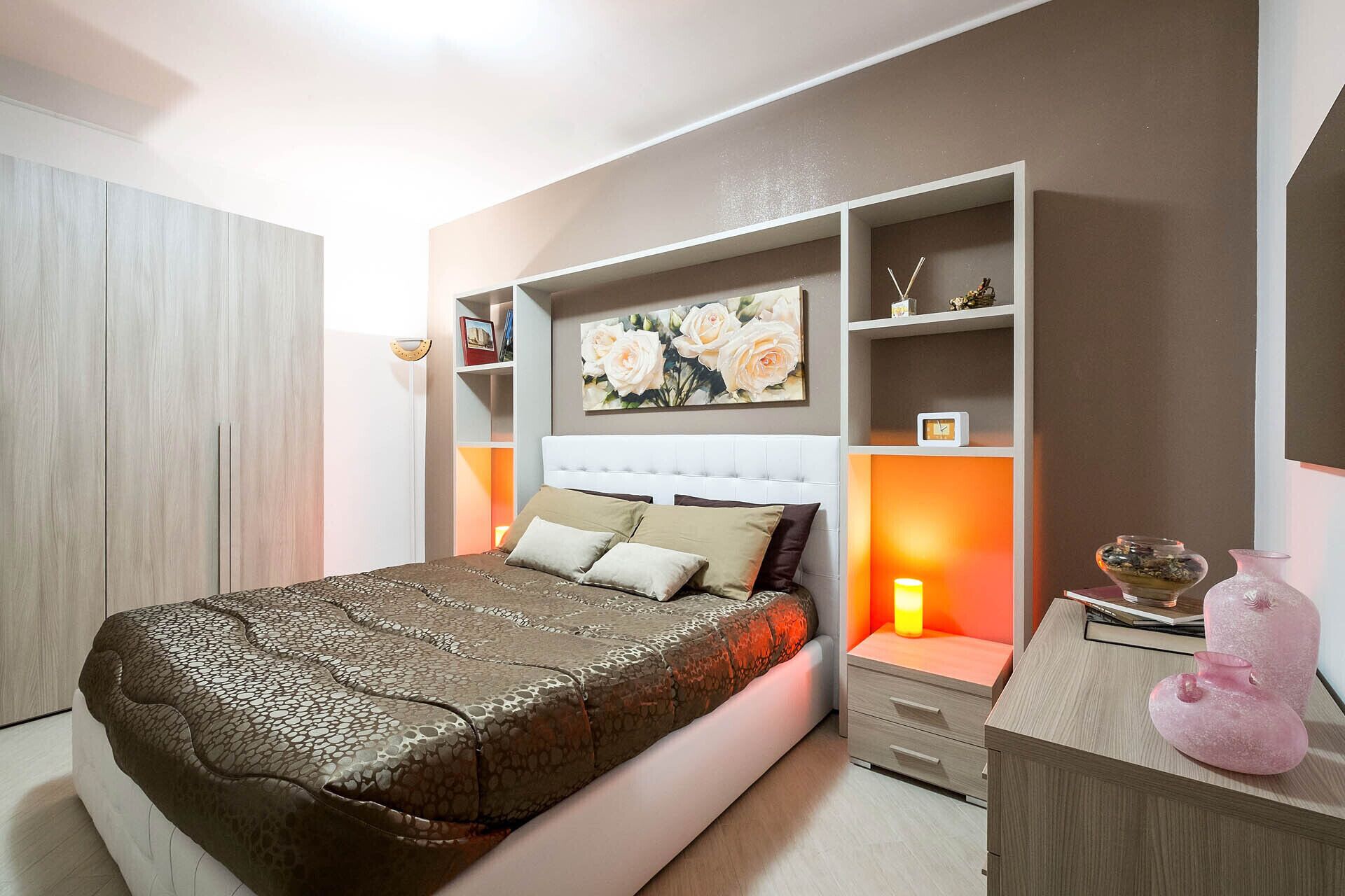 Un dormitorio con cama, mesitas de noche, armario y estante con objetos decorativos.