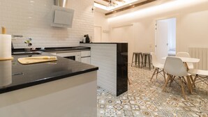 A modern kitchen with white subway tiles, a black countertop, and a patterned floor. There is a dining area with white chairs and a table.
