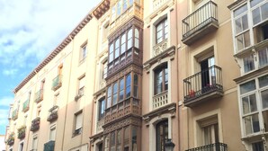 A multi-story building with ornate balconies, large windows, and a street in front.