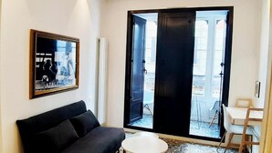 A modern living room with a black sofa, a small round table, and a large sliding glass door leading to an outdoor area.