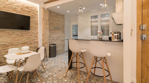 A modern kitchen with a white backsplash, wooden accents, and a dining area with white chairs and a tiled floor.