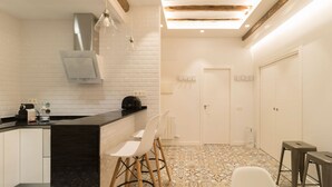 A modern kitchen with white cabinetry, a black countertop, and a patterned tile floor. There are two bar stools and a white chair.