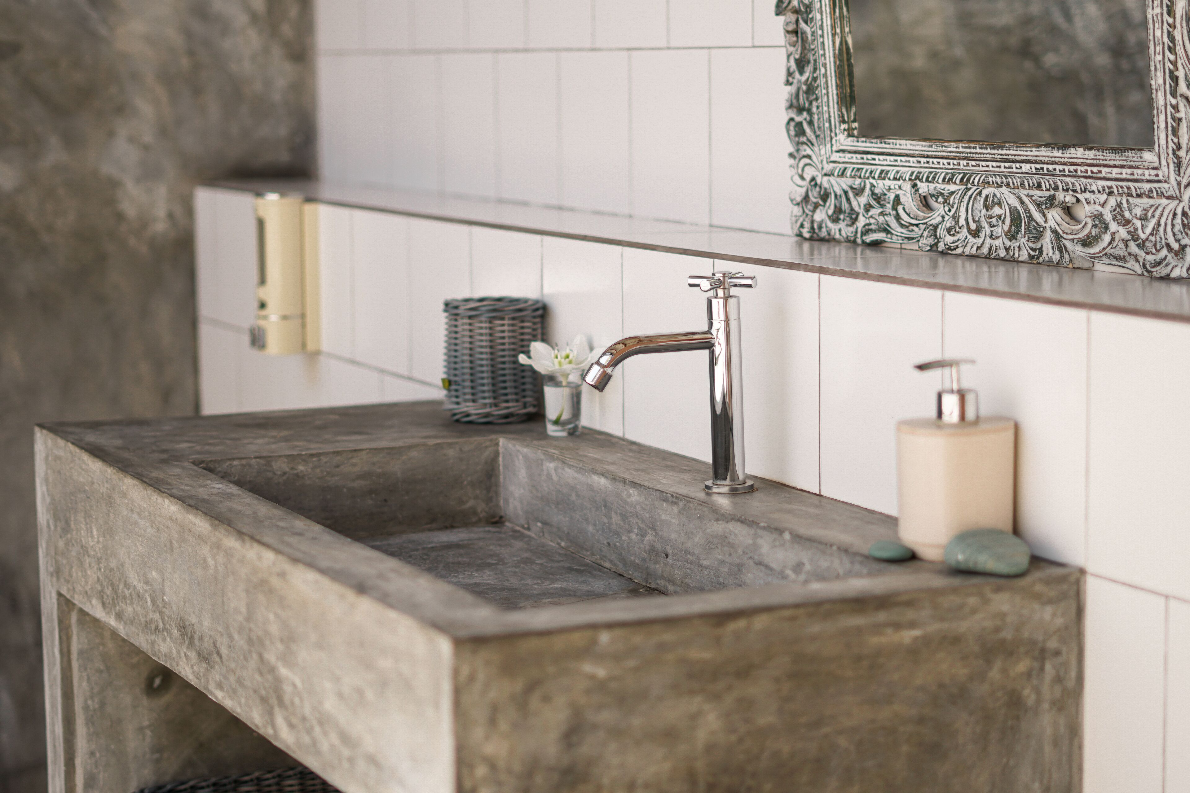 Un baño con un lavamanos de piedra rectangular, un espejo con un marco ornamentado y un dispensador de jabón.