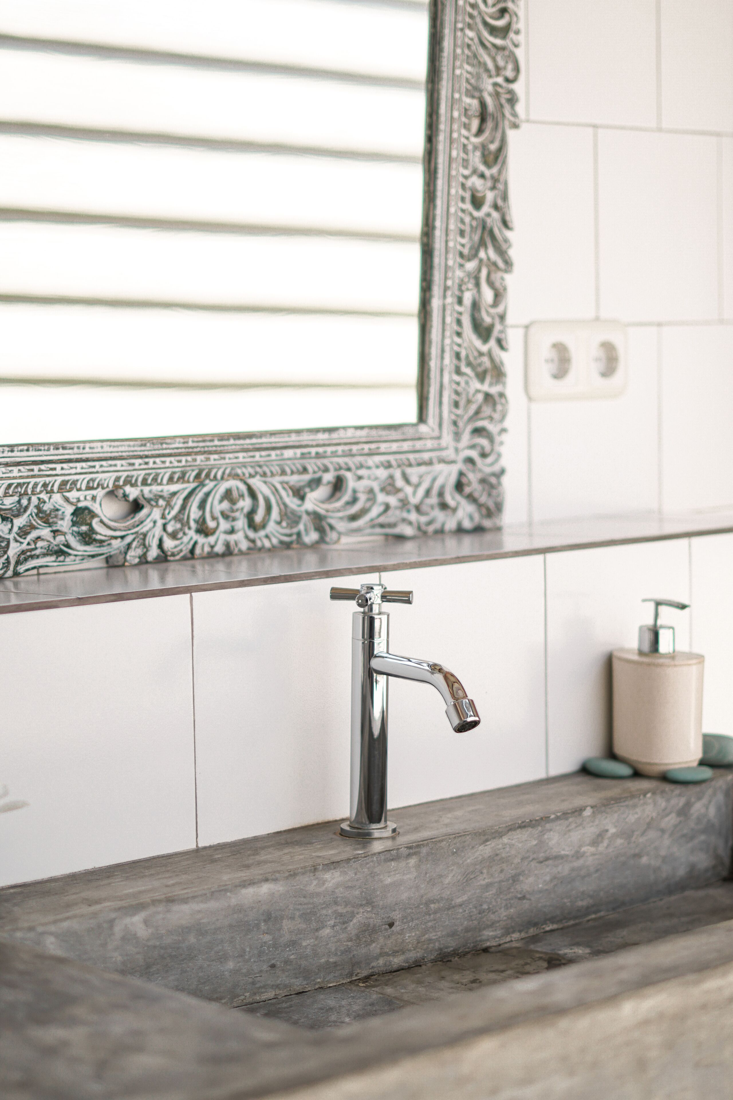 A bathroom with a modern sink, a decorative mirror, and a soap dispenser.