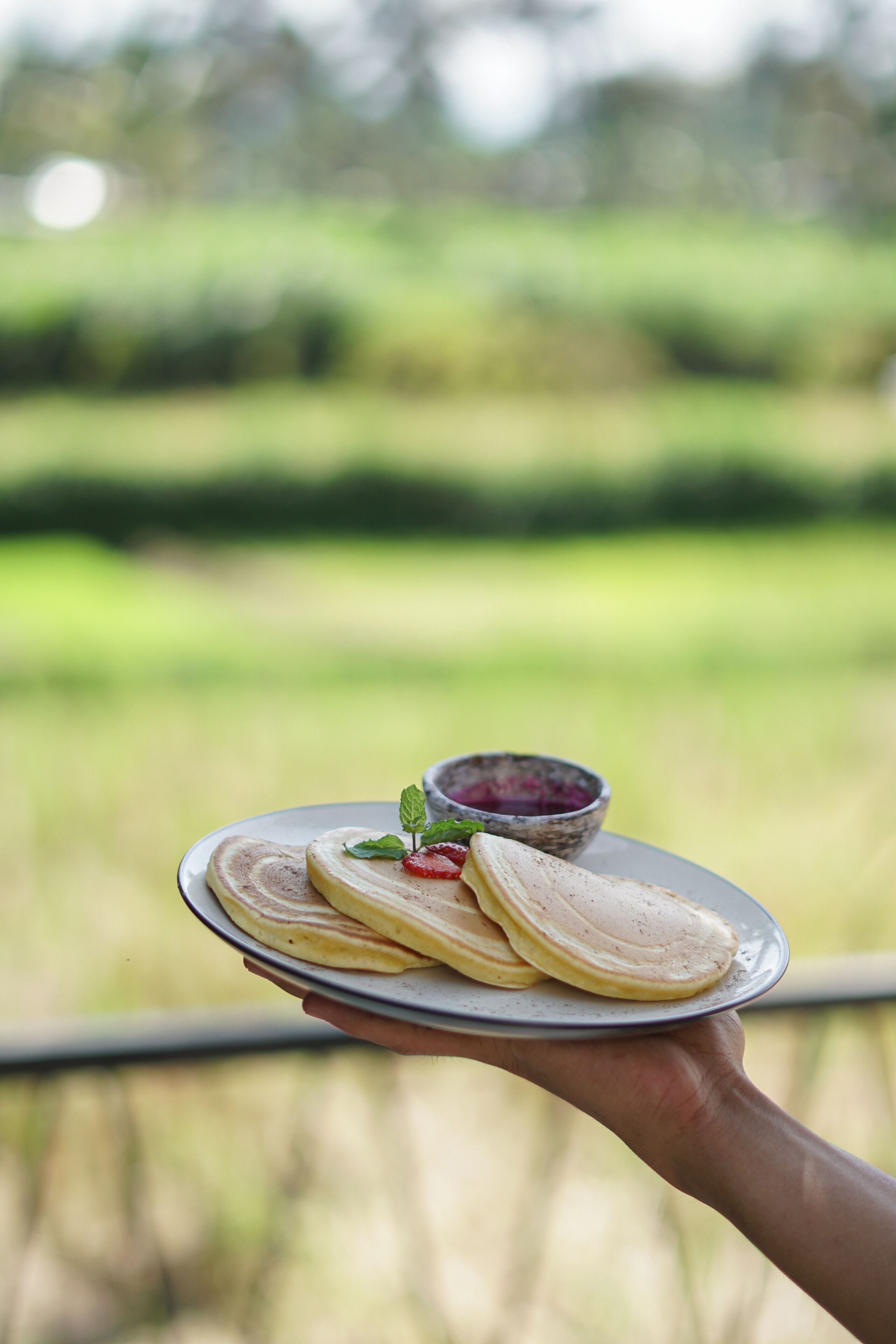 Una mano sostiene un plato con tortitas y un cuenco pequeño de mermelada.